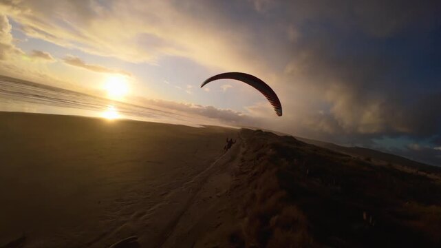 Paraglider flying above coastal sand dunes at sunset in New Zealand