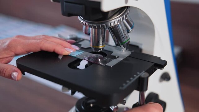 Laboratory technician adjusting microscope slide for medical analysis in clinical research facility.