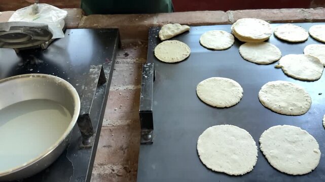 Guatemalan woman preparing handmade corn tortillas from fresh masa dough and placing them on hot griddle. Traditional cooking process showcasing local cuisine, culture and authentic food preparation.