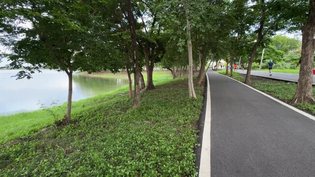 Horizontal stationary footage of an active park running track with multiple joggers running past the side of the camera lens