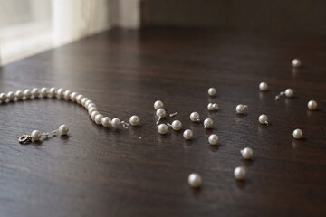 Fototapeta premium A single strand of pearls breaking apart on a dark table, pearls scattering.