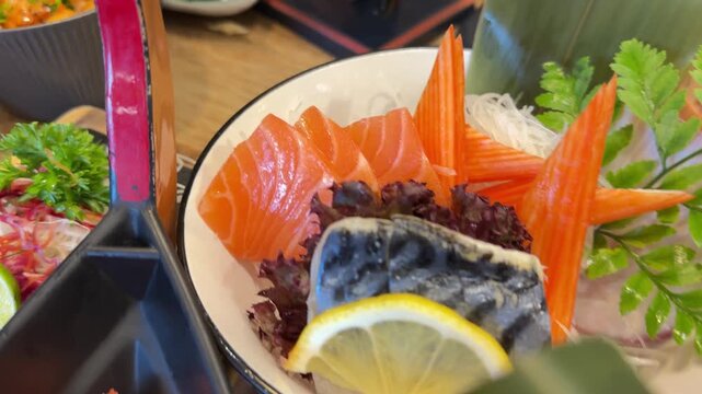 Horizontal video panning smoothly across a wooden table filled with multiple Japanese dishes including salmon don tuna sashimi and crab sticks