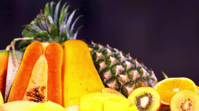 Close up macro shot of fresh organic tropical fruits including pineapple papaya kiwi and orange on a dark background in studio