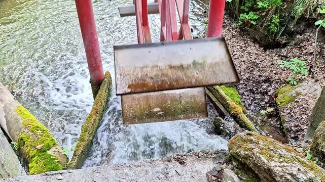 Historic water mill sluice gate channels a fast flowing stream through a lush natural setting. Rushing water, rustic engineering, and tranquil countryside create a timeless scene
