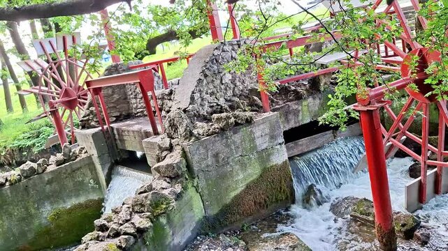Water flows through a mill sluice and spillway surrounded by stonework and greenery. Cascading currents, textured surfaces, and peaceful outdoor scenery create a calming atmosphere