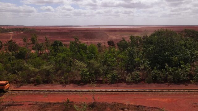Aerial static drone view of a diesel mining train transporting bauxite ore along railway tracks near Weipa, Cape York, Australia. Active open mining operation visible in background.