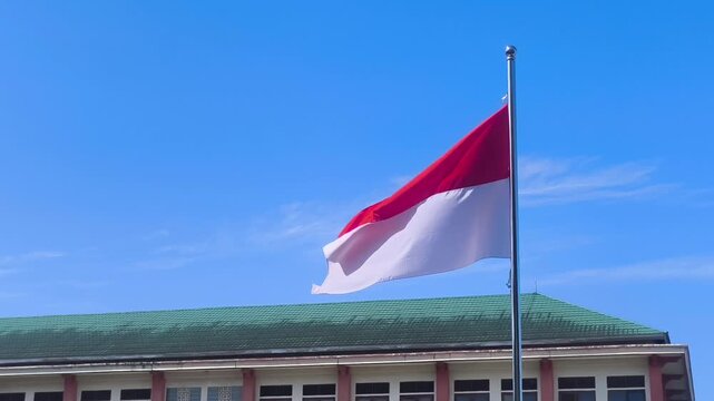 The Indonesian red and white flag flutters proudly on a flagpole under a clear blue sky.