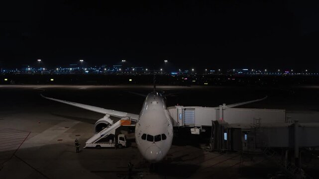 Commercial airplane docked at jet bridge on airport tarmac at night with city lights in background China