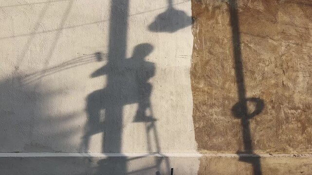 Silhouette shadow of a utility worker seated on an electrical pole while performing maintenance work, highlighting infrastructure services, skilled labor and urban utility operations