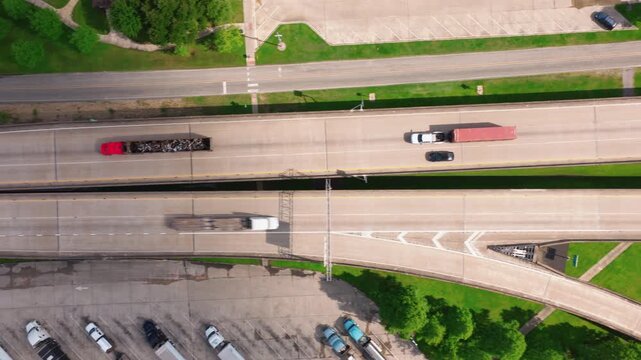 Top-down drone view of a red semi truck hauling an open trailer full of scrap metal along an I-10 interstate in Louisiana on a bright summer day.
