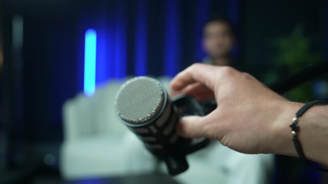 Hand gestures thumbs up near microphone in relaxed studio interview setting, adjusting mic stand