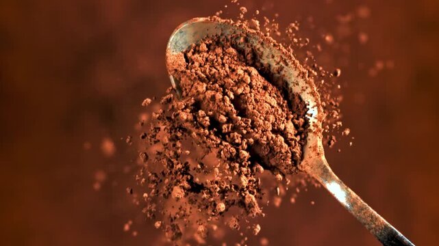 Close up shot of a metal spoon lifting ground aromatic brown coffee powder with fine particles scattering against dark background