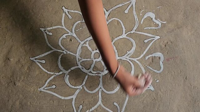 Woman drawing a traditional Rangoli pattern on the floor using rice and water mixed white paint. This beautiful handmade floral design is commonly created during Hindu festivals, religious ceremonies