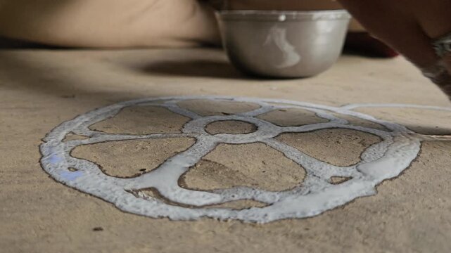 Woman drawing a traditional Rangoli pattern on the floor using rice and water mixed white paint. This beautiful handmade floral design is commonly created during Hindu festivals, religious ceremonies