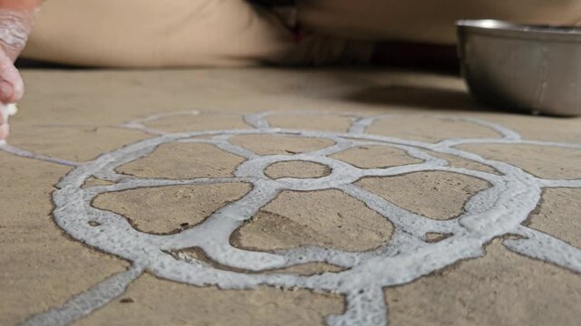 Woman drawing a traditional Rangoli pattern on the floor using rice and water mixed white paint. This beautiful handmade floral design is commonly created during Hindu festivals, religious ceremonies