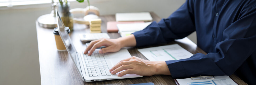 Adult professional working on laptop at office desk analyzing business reports and documents in modern workspace
