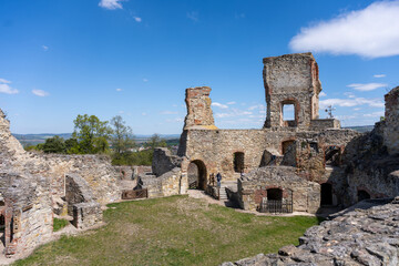 Fototapeta premium Visitors walk through the historic Boskovice Castle ruins on a sunny day in Czechia. The ancient stones stand firm amid green grass and blue skies.