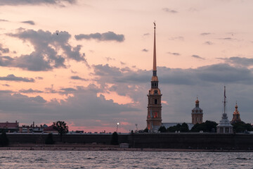Fototapeta premium Soft pastel sunset over Peter and Paul Fortress and cathedral spire in Saint Petersbur, reflected on the Neva River. Calm evening atmosphere with historic architecture, waterfront silhouettes