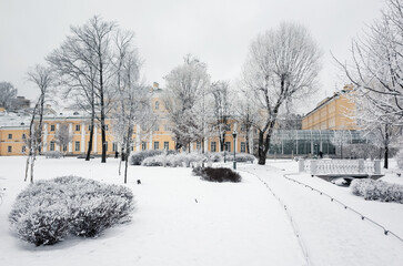 Fototapeta premium A scenic snow-covered park featuring frosted trees and a historic yellow buildings, evoking a serene and magical winter atmosphere in an urban setting of The Polish Garden, Saint-Petersburg, Russia