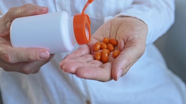Orange vitamin capsules pouring from white plastic bottle into woman's hand. Concept of health, beauty and longevity. Daily supplementation, antioxidant coenzyme Q10, anti-aging and energy maintenance