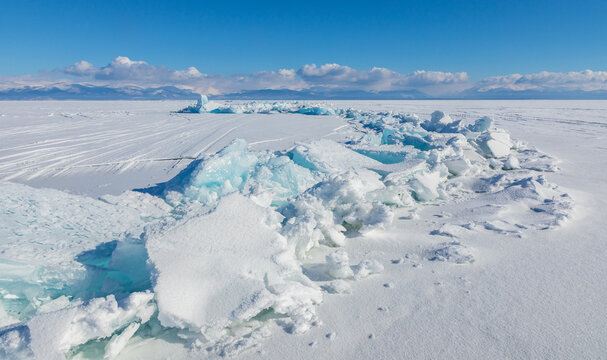 View of the frozen surface of Lake Baikal with jagged blue ice ridges and snow under a clear blue sky in Davsha, Buryatia, Russia.