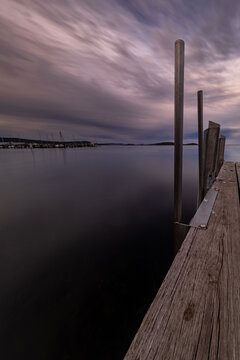 View of Princess Royal Sailing Club with a wooden pier extending into the calm waters of the bay under a dramatic cloudy sky in Little Grove, Western Australia, Australia.