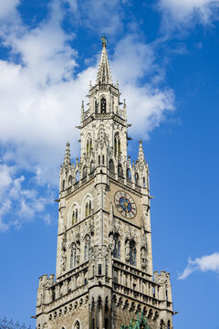 View of the ornate Gothic tower of the Neues Rathaus with its detailed clock face and stone carvings against a bright blue sky in Munich, Bavaria, Germany.