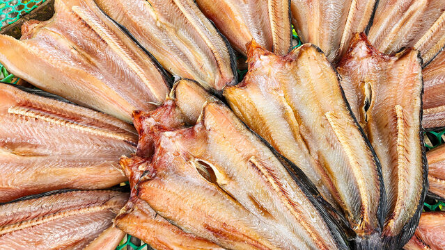 A top-down view of sun-dried striped snakehead fish split open and arranged in a circular pattern on a mesh tray at a traditional Thai market.