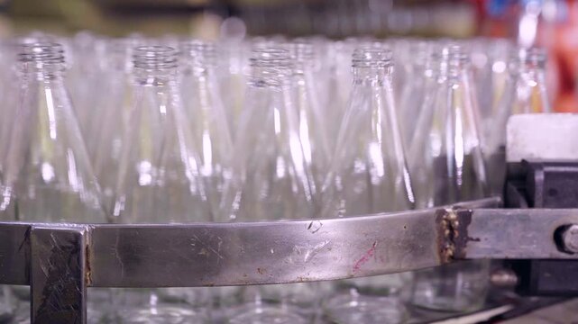 Row of empty glass bottles moving on a factory conveyor belt