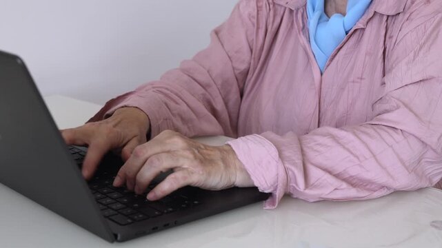 Mature woman working on a laptop at home. Close-up of senior hands typing on a keyboard for online work, email or remote communication.