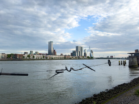 Rotterdam, Netherlands skyline with Erasmus Bridge, modern buildings over river, cloudy sky.
