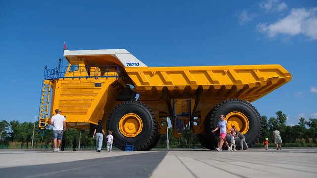 Minsk. Belarus. 09.08.2025 Huge yellow mining dump truck with people standing beside it. Tourism visiting outdoor industrial monument site. Transport engineering giant for heavy industry work.