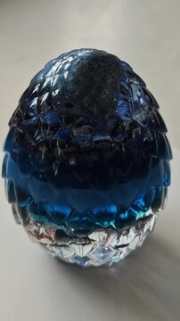 Blue Dragon Egg Orgone Generator Rotating Close Up, Handmade Epoxy Resin Orgonite Sculpture with Mystical Energy Aesthetic on White Marble Background