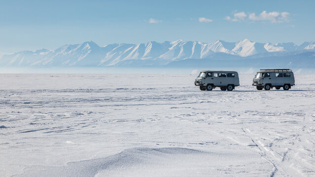 View of two UAZ Bukhanka vans on the frozen surface of Lake Baikal with snow-covered mountains in the background in Davsha, Buryatia, Russia.