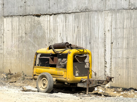 Aerial view of a yellow portable air compressor on a trailer parked against a concrete wall in Istanbul, Istanbul, Turkiye.