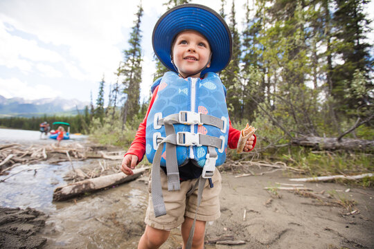 Happy toddler in a life vest exploring a riverbank
