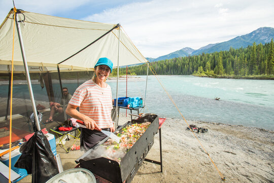 Happy woman cooking stir fry while camping by a river
