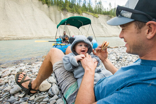 Father and baby enjoy a snack on a riverbank