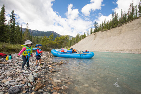 Kids in life jackets play by a mountain river