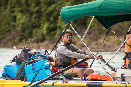 Bearded man rows a raft full of camping gear