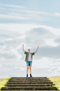 Teenage boy celebrating on top of outdoor steps beneath open sky