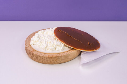 A crispy oblea wafer filled with fresh white cheese and topped with caramel spread, resting on a round wooden board.