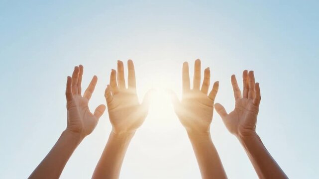 Two human hands reaching towards bright sun in clear blue sky with fingers spread wide open symbolizing hope and aspiration on sunny day