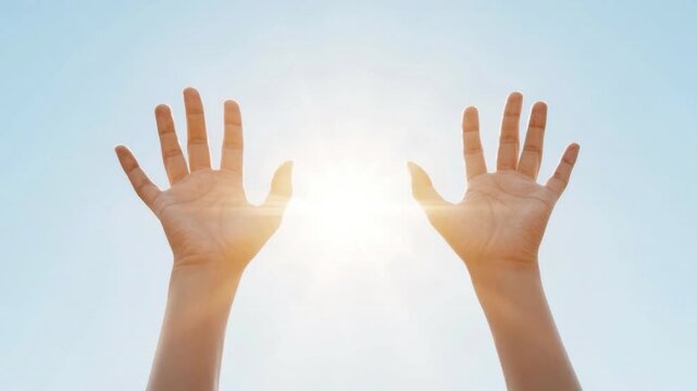 Two human hands raised up reaching towards bright glowing sunlight against clear blue sky symbolizing hope, freedom, and positivity