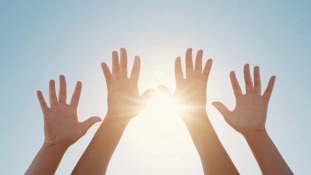 Diverse group of hands raised against bright clear blue sky with sunlight shining through fingers in outdoor setting