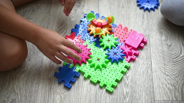 Bright plastic gear set arranged on floor while boy builds mechanism by hand. Gear toy demonstrates logical thinking, creativity, and engaging educational childhood activity at home.