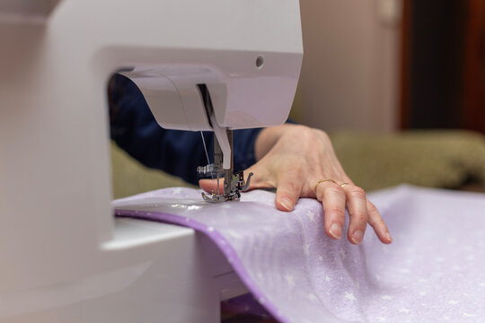 Close up of a woman's hands sewing light purple star-patterned fabric using a modern white sewing machine