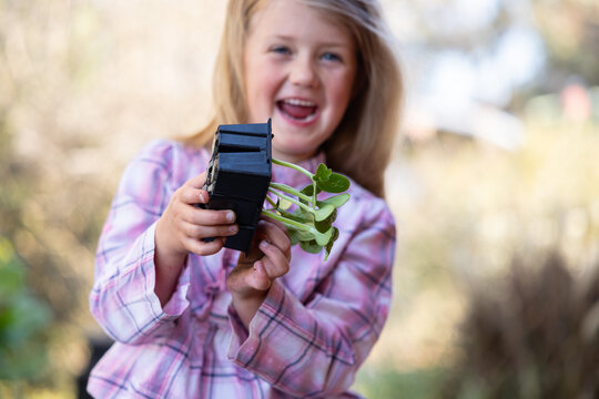 Child happily holding pot of green seedlings outdoors
