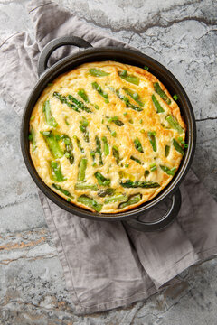 Savory baked frittata featuring asparagus and a fresh herb closeup in the skillet on the table. Vertical top view from above