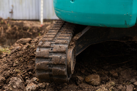 Close-up of small excavator&rsquo;s rubber track pressing into a mound of soil and rocks